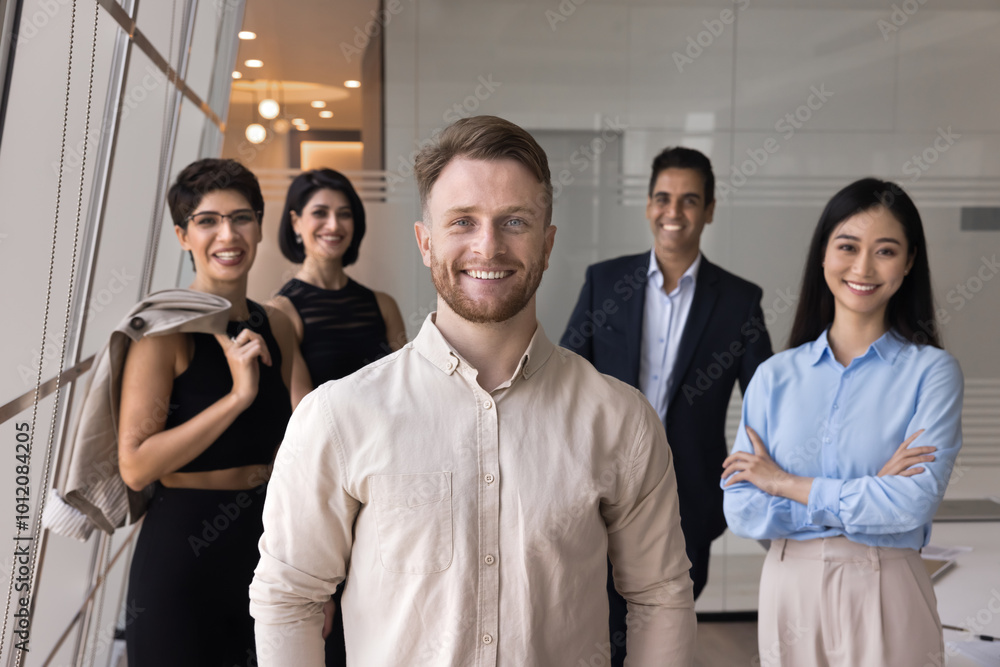 Happy handsome young business team leader man posing for portrait in front of diverse team. Positive project colleagues looking at camera, smiling, enjoying partnership, teamwork, meeting Happy handsome young business team leader man posing for portrait in front of diverse team. Positive project colleagues looking at camera, smiling, enjoying partnership, teamwork, meeting