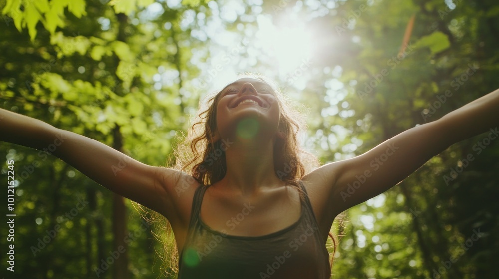 Naklejka premium A joyful woman with outstretched arms in a sunlit forest, embracing nature and freedom.