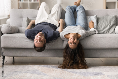 Wallpaper Mural Happy carefree young couple resting upside down on comfortable couch, lying with legs on back and heads hanging to carpeted floor, looking at camera, smiling, laughing, having fun Torontodigital.ca