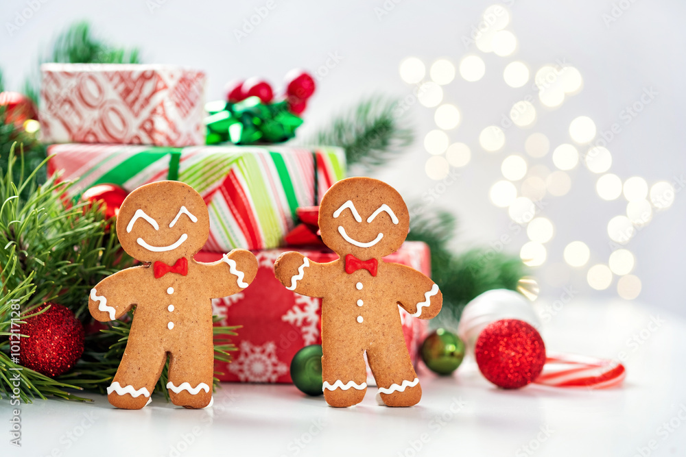 Two gingerbread men are smiling and standing next to a stack of presents Two gingerbread men are smiling and standing next to a stack of presents