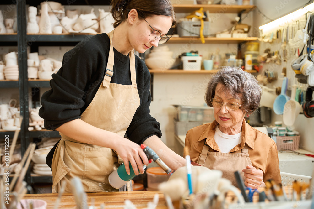 Fototapeta premium Young woman teaches elderly lady how to work with clay