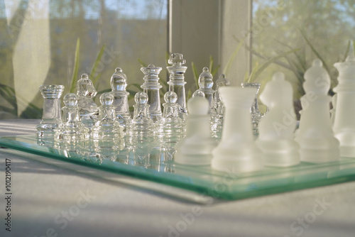 Glass chess on a white table in a bright, sunlit room. Space for text. The concept of hobby and leisure. Eye level view. photo