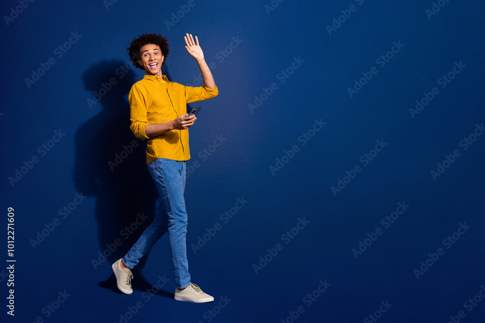 Full size photo of nice young man wave hi walk phone empty space isolated on dark blue color background