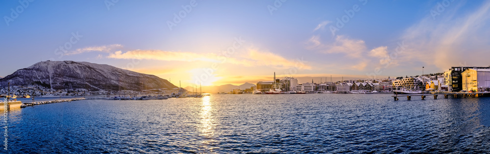 Fototapeta premium Panorama of Tromso harbor at sunset in winter, Norway. Scandinavian buildings and boats in port of Tromso and Storsteinen mountain. Snowy winter landscape in arctic circle town in far northern Norway