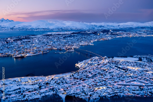 Aerial view of Tromso, Norway with city lights in winter from Storsteinen mountain at twilight. Tromsoya island with Tromso downtown, harbor, Sandnessundet bridge, fjord and mountains in polar night
