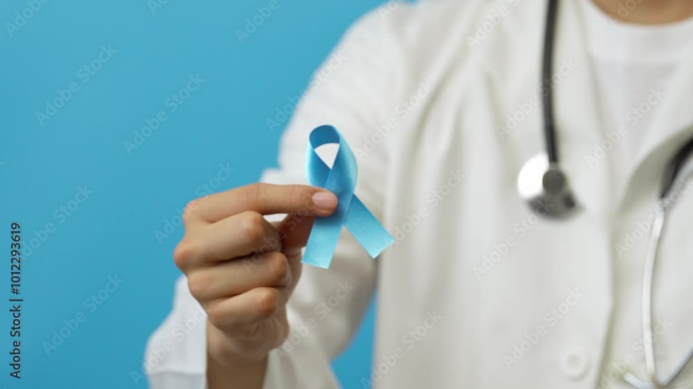 Young male doctor shows a blue ribbon, symbol of the fight against prostate cancer, human trafficking, the deaf community, blue background Young male doctor shows a blue ribbon, symbol of the fight against prostate cancer, human trafficking, the deaf community, blue background