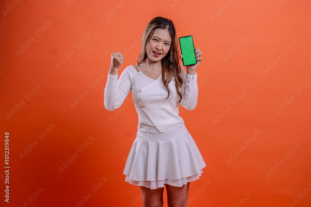 woman white top standing cheerful to camera both hands hold mobile phone screen, cellphone while clenched to the side isolated orange background. for technology, business, promotion, lifestyle concept woman white top standing cheerful to camera both hands hold mobile phone screen, cellphone while clenched to the side isolated orange background. for technology, business, promotion, lifestyle concept