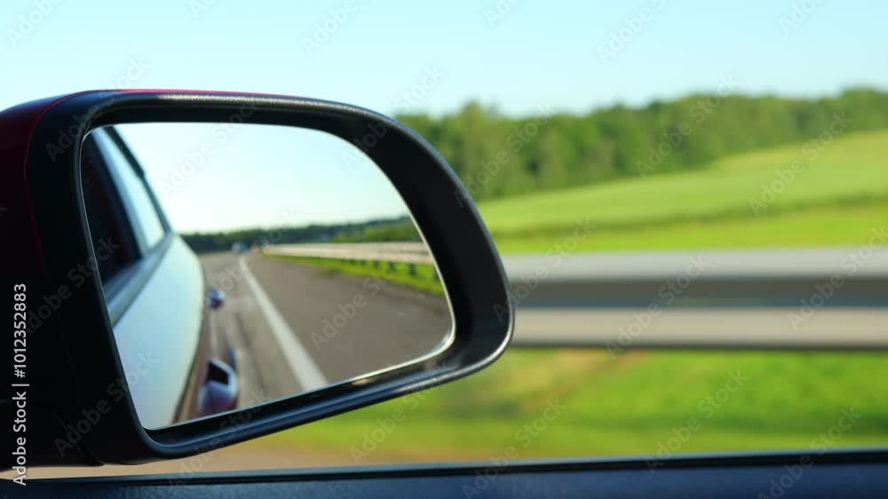 Red automobile in motion. View in the rear view side mirror of a auto, driving a red car along the track Red automobile in motion. View in the rear view side mirror of a auto, driving a red car along the track