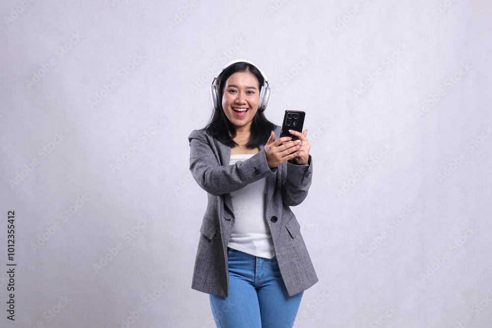 Beautiful adult office woman happy wearing headphone headset and holding mobile phone streaming video wearing suit isolated on white background. lifestyle, education, entertainment, technology concept Beautiful adult office woman happy wearing headphone headset and holding mobile phone streaming video wearing suit isolated on white background. lifestyle, education, entertainment, technology concept
