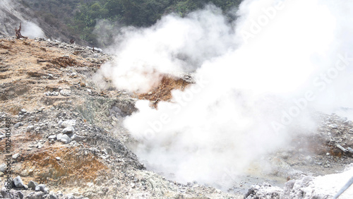 A breathtaking view of an active volcanic crater emitting thick white steam, signaling geothermal activity. The rugged terrain and rising vapors capture nature's raw power