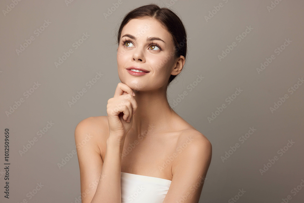 Beautiful young woman smiling and posing with her hand on her chin, looking to the side on a gray background Beautiful young woman smiling and posing with her hand on her chin, looking to the side on a gray background