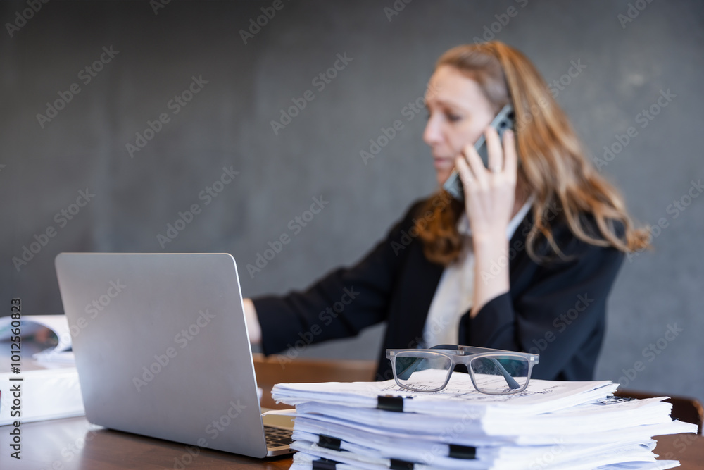 Close-up of Glasses on a Desk as Businesswoman Manages Work on Phone and Laptop in a Corporate Office