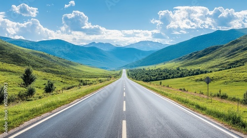 A straight asphalt road through green mountain terrain, under a clear sky with light, scattered clouds on a sunny afternoon.