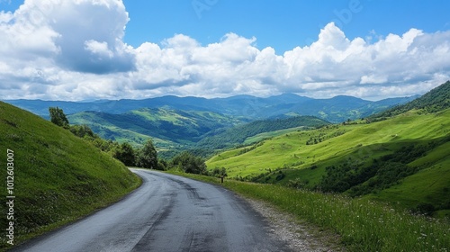 An asphalt road winding through green mountain valleys, with a clear sky and soft white clouds on a sunny, bright day.