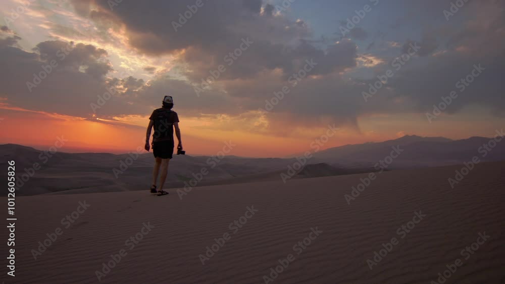 Hiker explores serene desert dunes at sunset with camera in hand Hiker explores serene desert dunes at sunset with camera in hand