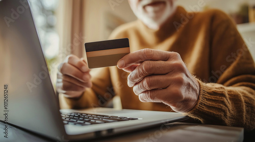 An elderly man is seen holding a credit card while using a laptop, symbolizing the vulnerability of seniors to online scams.