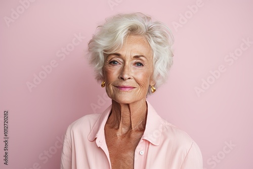 Portrait of a beautiful senior woman posing against a pink background.