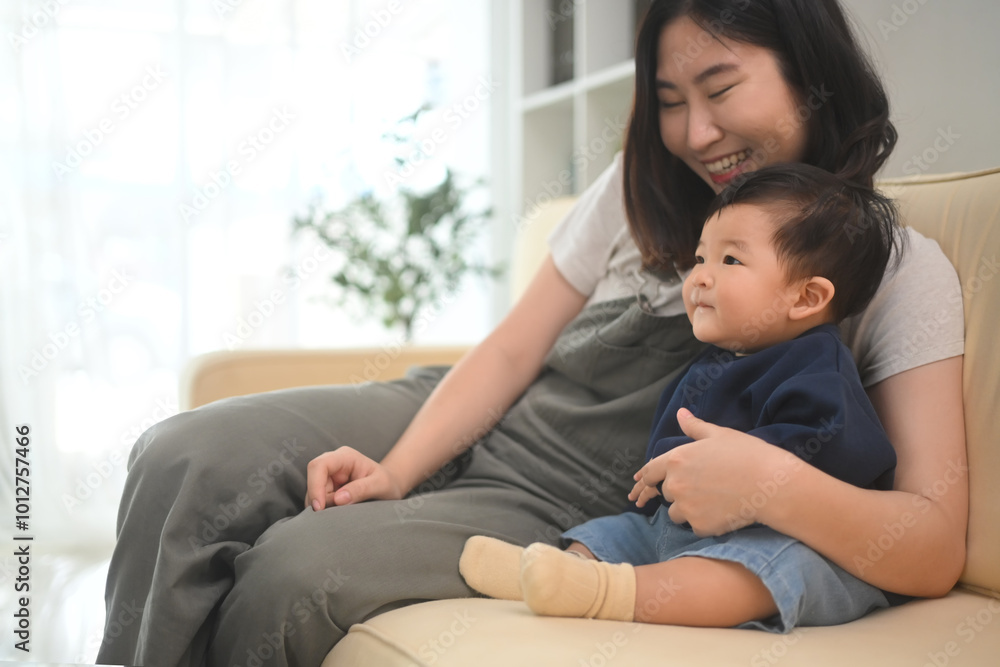Happy young mother playing cute little boy on sofa at home. Childhood and nurturing care concept Happy young mother playing cute little boy on sofa at home. Childhood and nurturing care concept