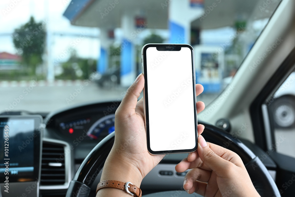 Close up shot of woman sitting in car holding smartphone on the background of a gas station Close up shot of woman sitting in car holding smartphone on the background of a gas station