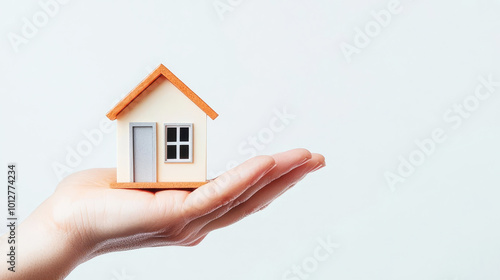 A hand holds a small model house, symbolizing home ownership, real estate, or property management.