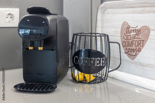 A modern coffee machine with a wire capsule holder and a decorative tray that says 