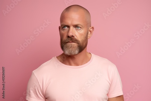 Portrait of serious bearded mature man in pink t-shirt, looking at camera, posing isolated over pink background.