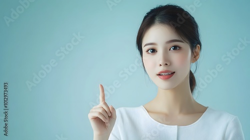 Asian woman presenting and pointing with copy space against a light blue background, showcasing beauty, confidence, and elegance