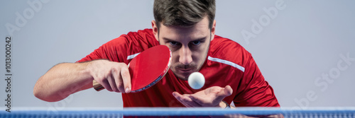 A man in a red shirt is playing ping pong. He is holding a paddle and is about to hit a ball photo