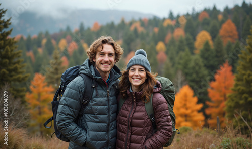 A young couple is hiking in the mountains, with a backdrop of vibrant fall foliage. They are both smiling and appear happy to be enjoying the outdoors together.