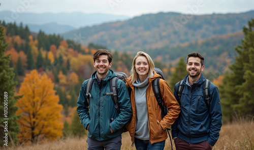 Three friends are standing on a hilltop, looking towards the camera and smiling as they pose for a photo during their hike in the autumn mountains.