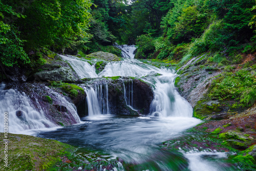 Multi-tiered waterfall cascades gently over moss-covered rocks in Japan photo