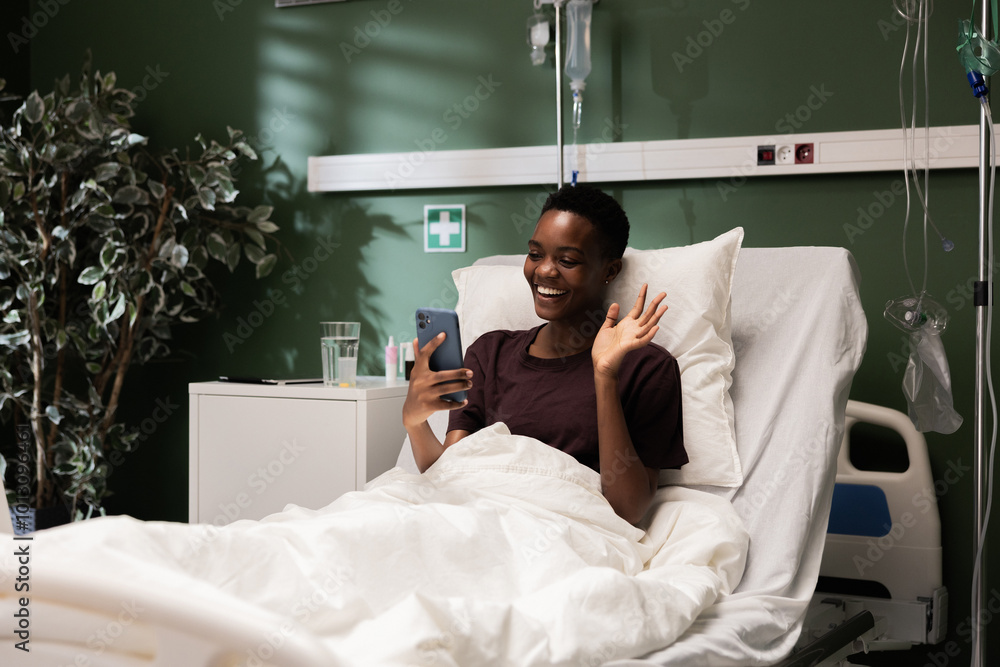 In the hospital room, a young African patient relaxes with her phone, watching a movie or a TV show.