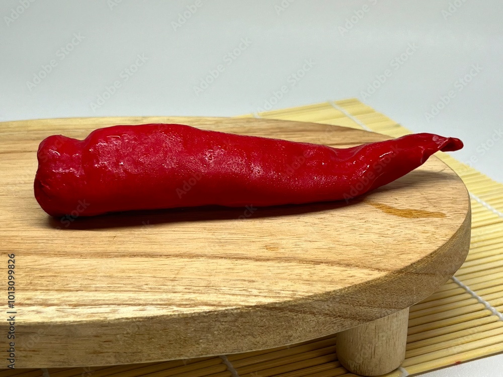 A red chili pepper placed on a wooden cutting board, showcasing its vibrant color and shape. A red chili pepper placed on a wooden cutting board, showcasing its vibrant color and shape.