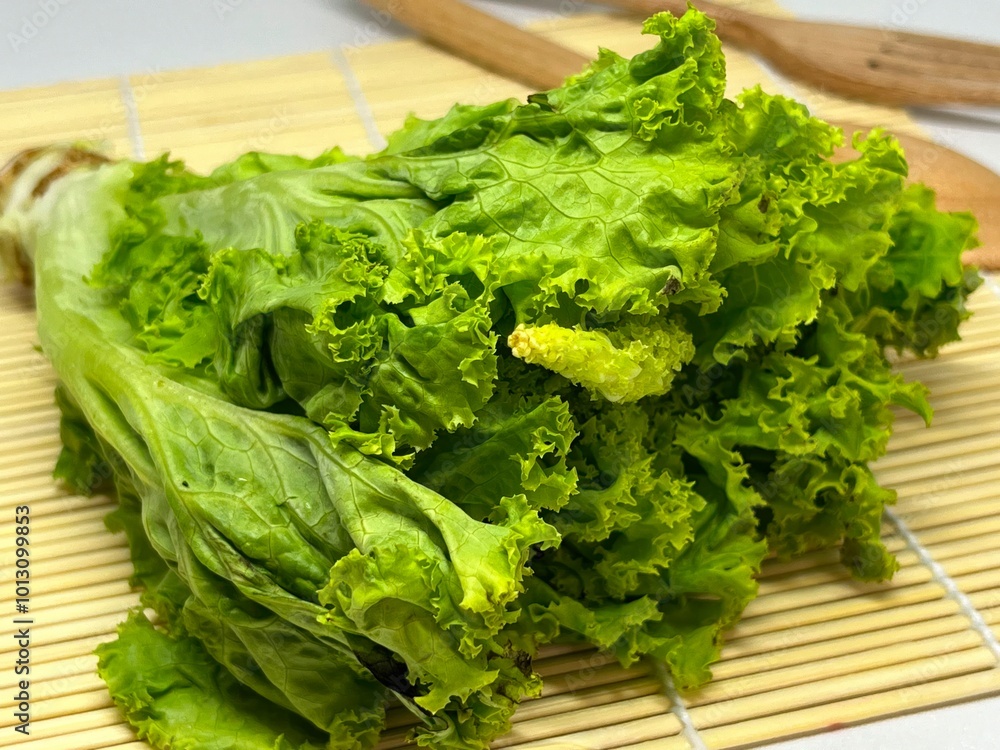 A bunch of fresh, green lettuce with curled leaves on a bamboo mat.