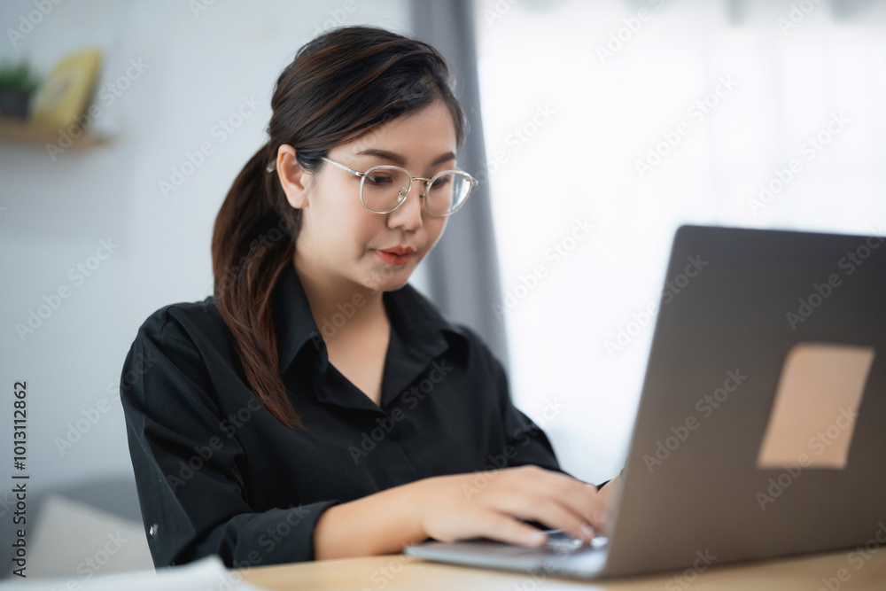 Asian woman wearing glasses is typing on a laptop. She is focused on her work and she is in a serious mood Asian woman wearing glasses is typing on a laptop. She is focused on her work and she is in a serious mood