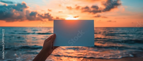 A hand holds a blank card against a stunning sunset by the ocean, capturing a perfect moment of tranquility and creativity.