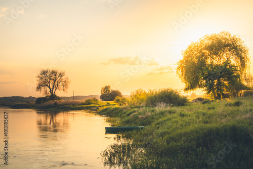 A landscape of the lake surrounded by the forest. Small lonely fishing boat at the shore. Golden hour. 