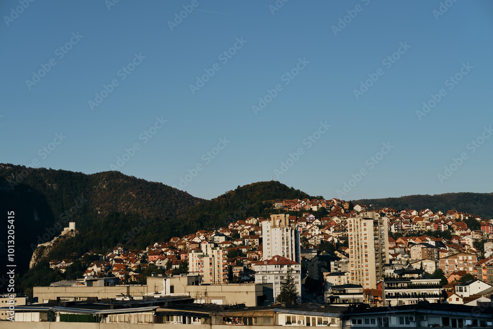 View of the old mountain houses with red tiled roofs and high-rise buildings in the Yugoslavian style. Small town Uzice in the south of Serbia. Clear blue morning sun. View of the old mountain houses with red tiled roofs and high-rise buildings in the Yugoslavian style. Small town Uzice in the south of Serbia. Clear blue morning sun.
