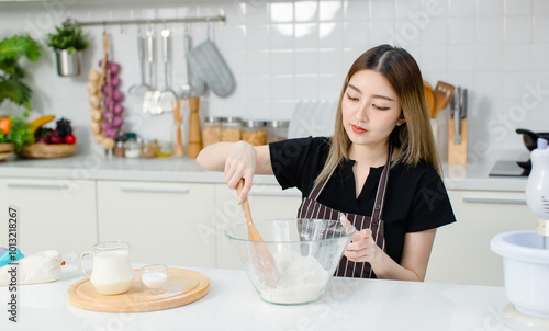 Young happy Asian beautiful woman, female wearing aprons intends to knead the dough mixing for baking cakes and making homemade bread and desserts. Lifestyle enjoy weekends cooking in kitchen at home