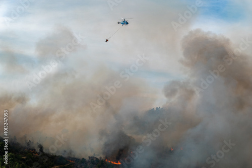 Helicóptero no combate a um incêndio florestal que deixa nuvens de fumo no ar photo