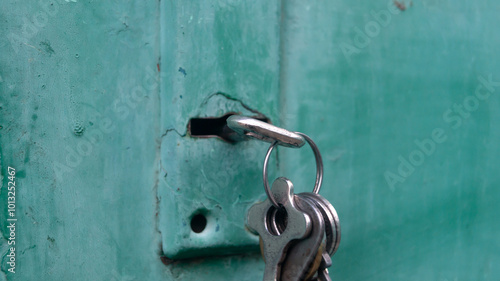 Close-up of a key inserted into the lock of a green metal door. Close-up of a bunch of keys hanging from a key inserted into the lock of a metal door
