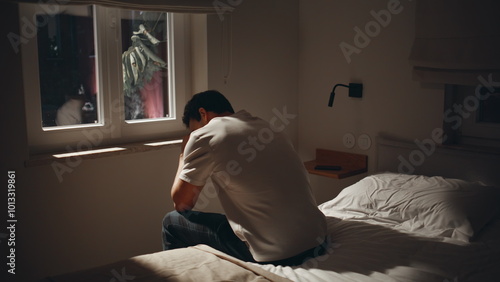 Exhausted guy suffering insomnia at dark bedroom. Depressed man sitting home bed