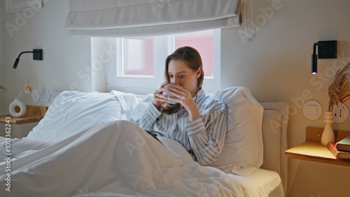 Lazy girl drinking coffee in cozy bed at morning. Calm woman reading tablet