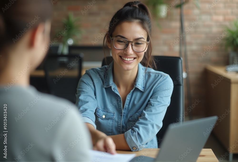 A woman wearing glasses and a denim shirt works on her laptop in a modern office, smiling while typing. A woman wearing glasses and a denim shirt works on her laptop in a modern office, smiling while typing.