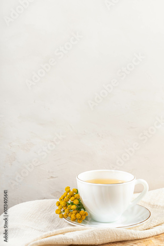 White cup on saucer with tansy decoction, tansy flowers on white napkin. Herbal medicine. Copy space photo