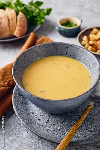 Bowl of potato soup puree with croutons, parsley and ground red pepper, and spoon on the plate.