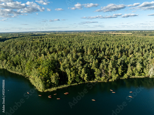 Aerial drone view of people kayaking on a lake surrounded by green forest. Kulka Reserve, Masuria, Poland. Sailing in red kayaks in the Masurian Lake District. Lake Lesk in the Kulka Reserve in Poland photo