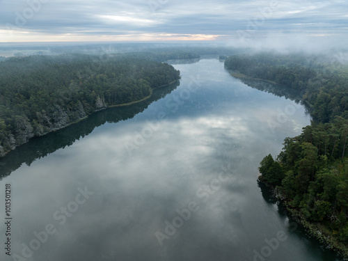 Aerial drone view of a lake surrounded by green forest. Big lake in the fog and clouds. Lake in the Masurian Lake District. Lake Lesk in the Kulka Reserve in Poland. Kulka Reserve, Masuria, Poland.