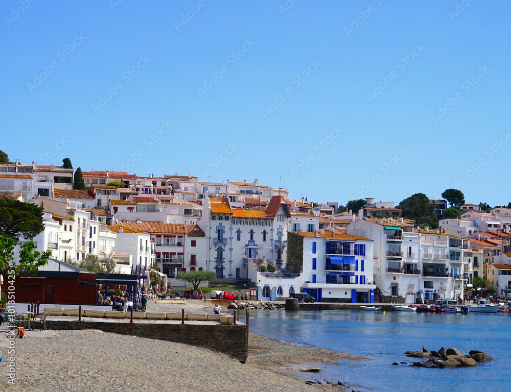 Obraz premium view along the promenade of Cadaqués, to the beautiful white houses, Port Alguer and the turquoise water of the Mediterranean Sea, mountains of the Pyrenees behind, Girona, Catalonia, Spain