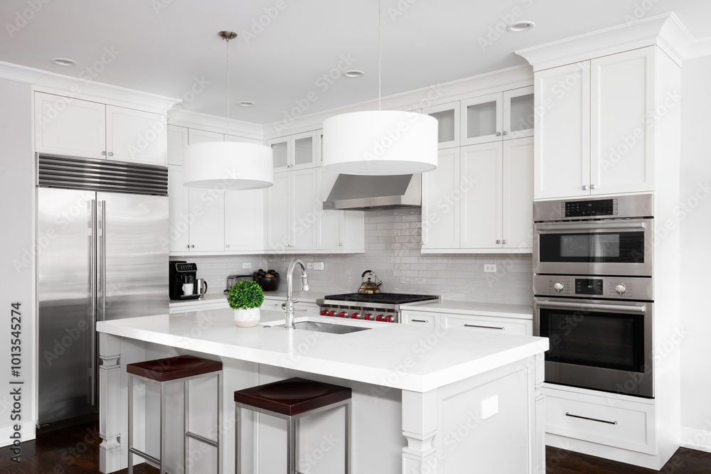 A white kitchen with pendant lights hanging above a large island, stainless steel appliances, and a grey subway tile backsplash. No brands or labels. A white kitchen with pendant lights hanging above a large island, stainless steel appliances, and a grey subway tile backsplash. No brands or labels.